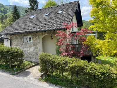 a stone house with a balcony and trees at Creek House Bohinj in Bohinj