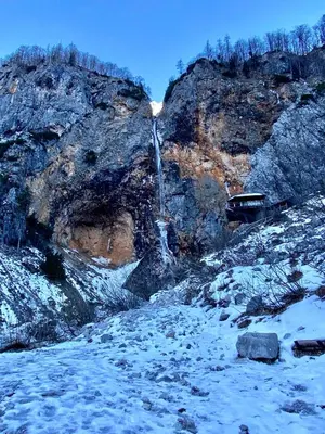 a waterfall on the side of a mountain with snow at Apartment Mandy in Rečica ob Savinji