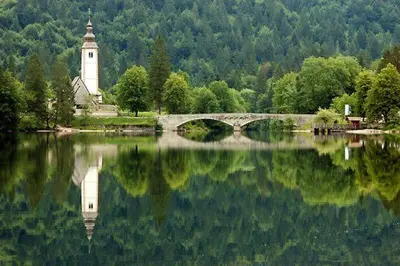 a bridge over a lake with a church and a clock tower at Villa Polje in Bohinj