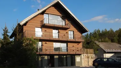 a large wooden house with a balcony and a car at Bed & Breakfast Base Camp in Križe