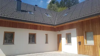 a white building with a wooden roof and a door at LARCH HOUSE in Cerklje na Gorenjskem