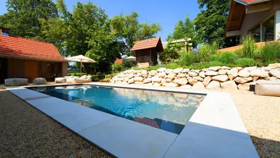 a swimming pool in a backyard with a rock wall at Premium Gardenguesthouse Mlinar with Pool & Sauna in Fokovci