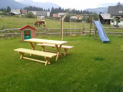 a picnic table and a playground with a slide and a cow at Apartments Bor in Bohinj