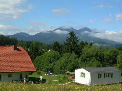 a house in a field with mountains in the background at Apartment Rozika in Slovenj Gradec