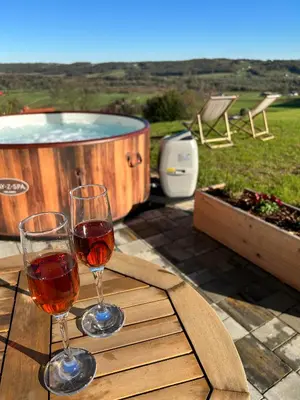 two glasses of wine sitting on a table with a hot tub at Hiška pod črešnjo in Rogašovci