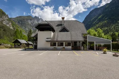 a building in a parking lot with mountains in the background at Metoja in Soča