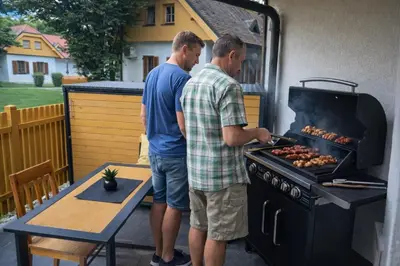 two men are cooking sausages on a grill at APARTMA MORAVSKE TOPLICE in Moravske Toplice