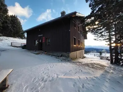 a cabin in the snow with footprints in the snow at Črnuški dom na Mali planini in Krivčevo