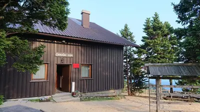 a small black building with a red sign on it at Črnuški dom na Mali planini in Krivčevo