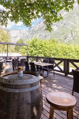 a wooden deck with tables and chairs and a barrel at Apartments Ukanc in Bohinj