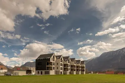 a building in a field with mountains in the background at Apartment Bela Bovec in Bovec