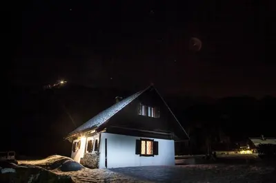 a small house with snow on the roof at night at Holiday House Damjana (Hiška Damjana), Ukanc, Bohinjsko jezero in Bohinj