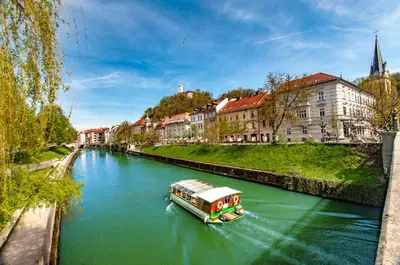 a boat traveling down a river in a city at Way to the Castle in Ljubljana