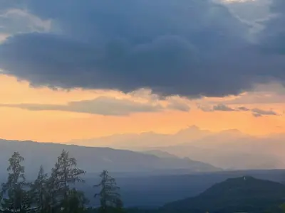a sunset over a mountain range with trees in the foreground at Elipa Cottage in Cerklje na Gorenjskem