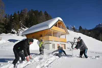 a group of people playing in the snow in front of a cabin at Cottage Osojnik - Alpine escape with Wellness in Solčava