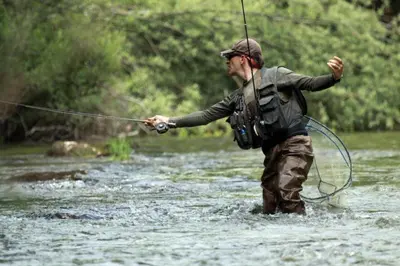 a man standing in a river holding a rod at Apartments BB in Bohinj