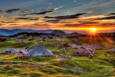 a group of huts on a hill with the sunset at Guest House Kraljev Hrib in Kamniška Bistrica