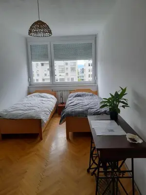 two beds in a room with a table and two windows at Room for women or couples in Ljubljana