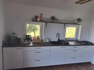 a kitchen with white cabinets and a sink and two windows at Vineyard cottage foggy sea in Semič