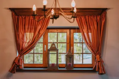 a window with orange curtains and a chandelier at Brunarica Dežno in Makole