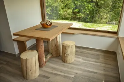 a wooden table and stools in front of a window at Hiška ob gozdu Lukez plac in Ljubno