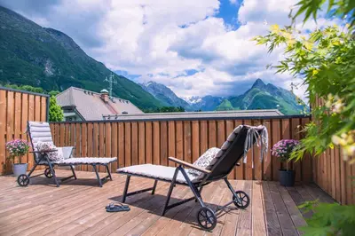 a stroller and a chair on a deck with mountains at Apartma Zeleni Biser in Bovec