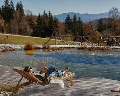two people laying on a bench with a laptop next to a pool at Glamping Zarja, Vipava Valley in Zoll