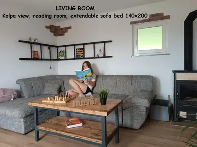 a woman sitting on a couch reading a book while playing chess at RELAX HOUSE Kolpa view Podzemelj in Gradac