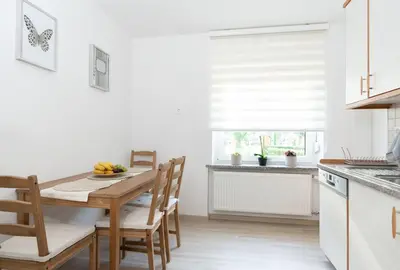 a white kitchen with a wooden table and chairs at Apartments BUMM in Ljubljana