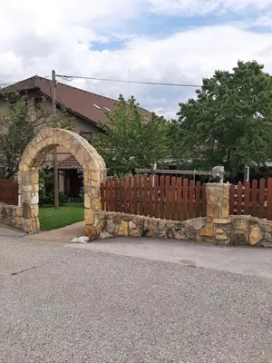 a stone fence with an arch in front of a house at Posestvo Rožengrunt pri Miheliču in Lokavec