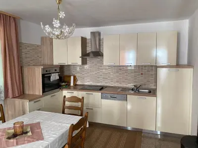 a kitchen with white cabinets and a table and a dining room at Apartma Medvedjek in Velika Loka