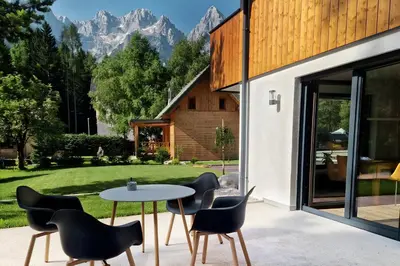 a patio with a table and chairs with mountains in the background at Hiša Oblak in Gozd Martuljek
