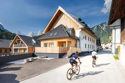 two people riding bikes down a street in front of buildings at Apartment MYSA, Nordic House, Kranjska Gora - Center in Kranjska Gora