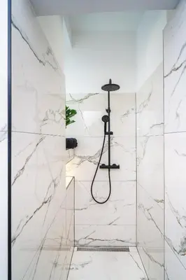 a bathroom with a shower with white marble walls at HL Apartments in Maribor