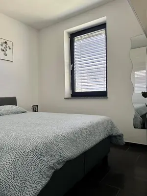 a white bedroom with a bed and a window at AURORA Apartment Banovci in Banovci
