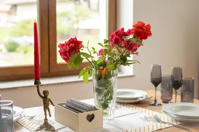 a vase with red flowers and a candle on a table at Aparthotel Hom at Vintgar in Zgornje Gorje