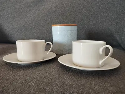 two white cups and saucers on plates next to a mug at Apartma Helena in Ajdovščina
