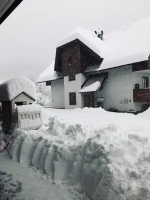 a snow covered house with a pile of snow at Sunrise Apartment in Rateče