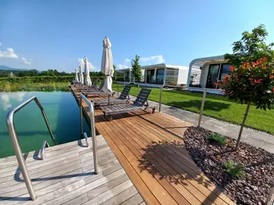 a wooden deck with chairs and umbrellas next to the water at Glamping Maleric with Natural Pool in Dragatuš