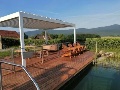 a wooden deck with chairs and a canopy over the water at Glamping Maleric with Natural Pool in Dragatuš