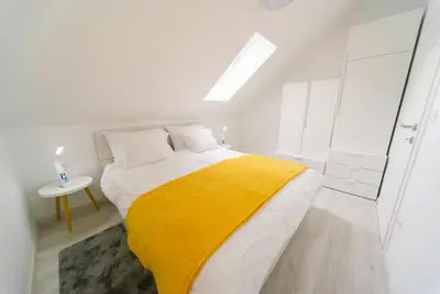 a white bedroom with a yellow blanket on a bed at Apartma RO-ZE in Bistrica ob Sotli
