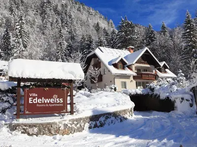 a house covered in snow with a sign in front at Vila Edelweiss Rooms&App Kranjska Gora in Kranjska Gora