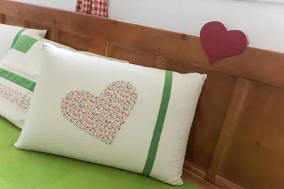 a pillow with a heart applique on a bed at Apartments Petacova Hiša in Kranjska Gora