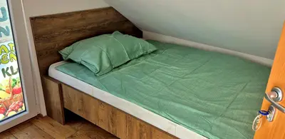a small bed with a green pillow in a room at Bled Lesce station rooms and depo in Lesce