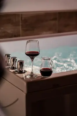 a glass of wine sitting on a table next to a tub at Wellness hiša Jelenov Grič in Mala Nedelja