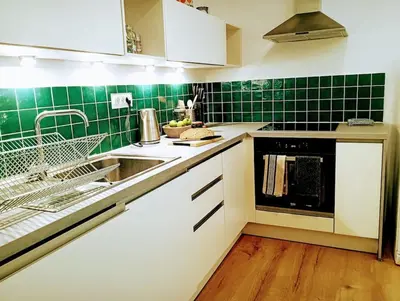 a kitchen with green tiled walls and white cabinets at Apartma Discovering Slovenia in Luče