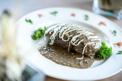 a white plate with a piece of meat with sauce at Hotel Tisa Pohorje in Pohorje