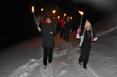 two women walking in the snow with torches at Apartments Lovec in Cerkno