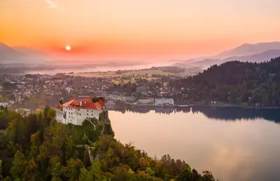 a castle on the edge of a lake at sunset at Apartments Hana Bled in Bled