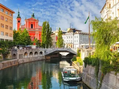 a boat on a river in front of a bridge at Fully equipped SIX BEDROOM HOUSE 15 kilometers from LAKE BLED - with a terrace, garden, playground, and parking in Kropa